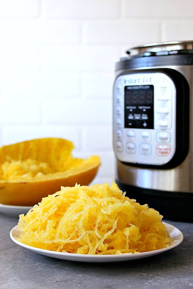 Side shot of cooked spaghetti squash on white plate, with Instant Pot in the background.
