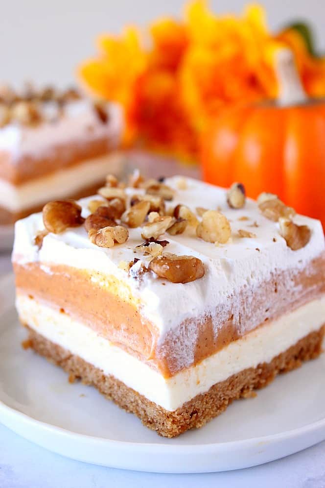 Close up shot of no-bake layered pumpkin lush dessert on white plate, with small pumpkin in background.