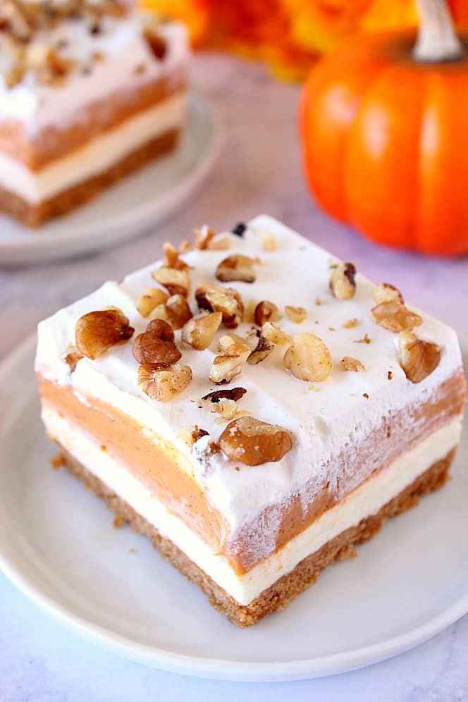 Overhead shot of layered pumpkin dessert on white plate, with pumpkin and another plate with dessert in background.