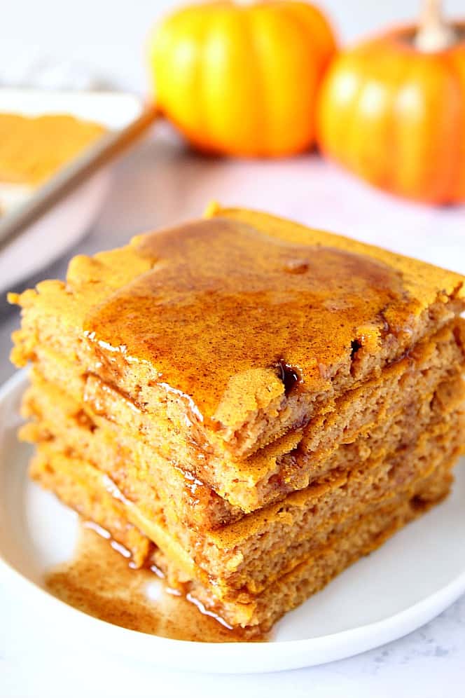 Pumpkin sheet pan pancakes stack on white plate, with pumpkins in the background.