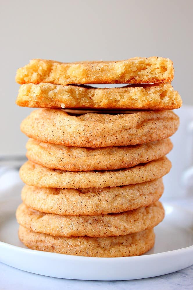 Close up shot of a stack of 7 cookies on white plate, with top cookie broken in half to show the center.