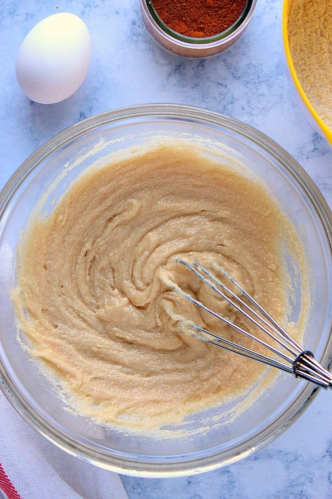 Overhead shot of melted butter whisked with sugar in a glass bowl with a wire whisk. 