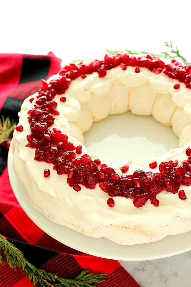 Side shot of Pavlova dessert with cranberry sauce on white cake stand. 