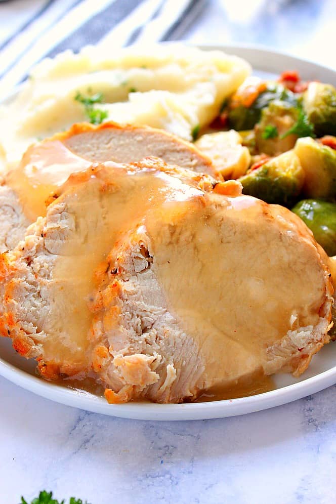 Close up shot of slices of boneless turkey breast with gravy, potatoes and Brussels sprouts on the side. 