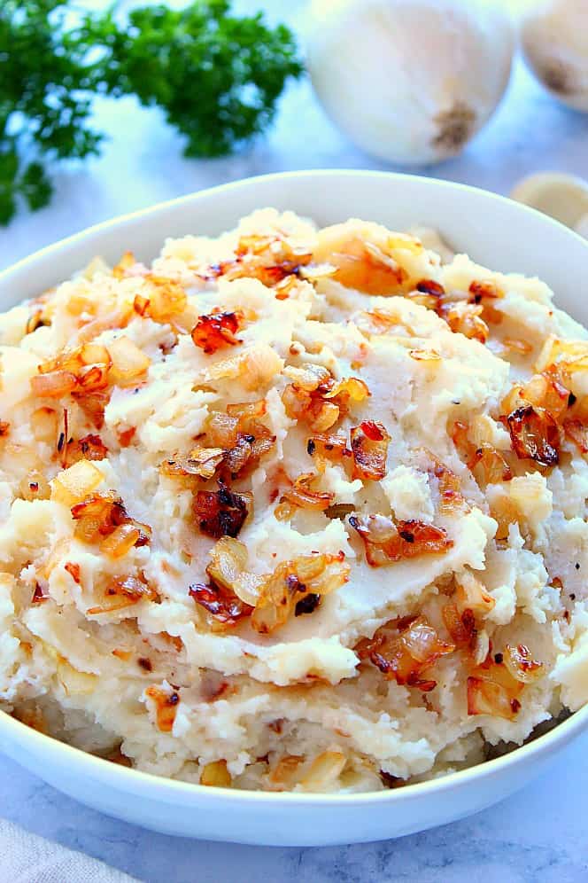 Side shot of mashed potatoes topped with caramelized onions, in white bowl. 