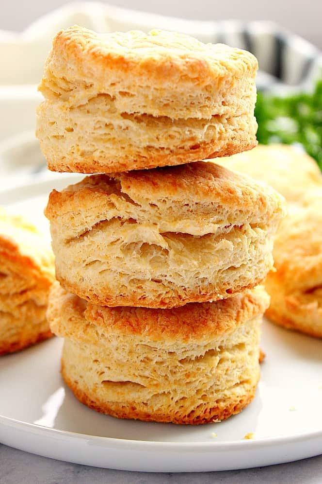 Three flaky biscuits stacked on each other on white plate. 