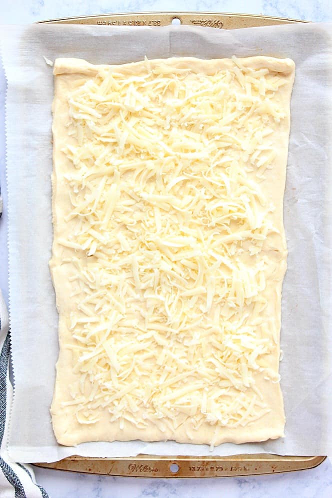 Overhead shot of crescent roll dough, rolled out on parchment paper and topped with cheese.
