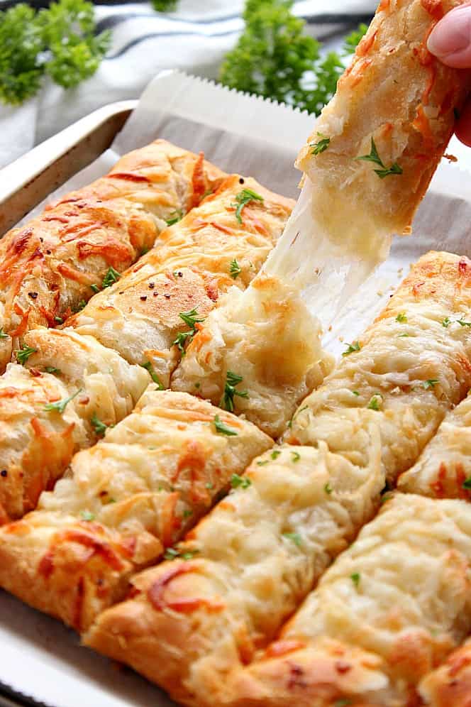 Garlic Butter Cheesy Breadsticks Recipe - the easiest way to make cheese-filled breadsticks, made with crescent roll dough, garlic butter, and cheese! Close up shot of breadsticks in pan, once pulled apart with cheesy center.