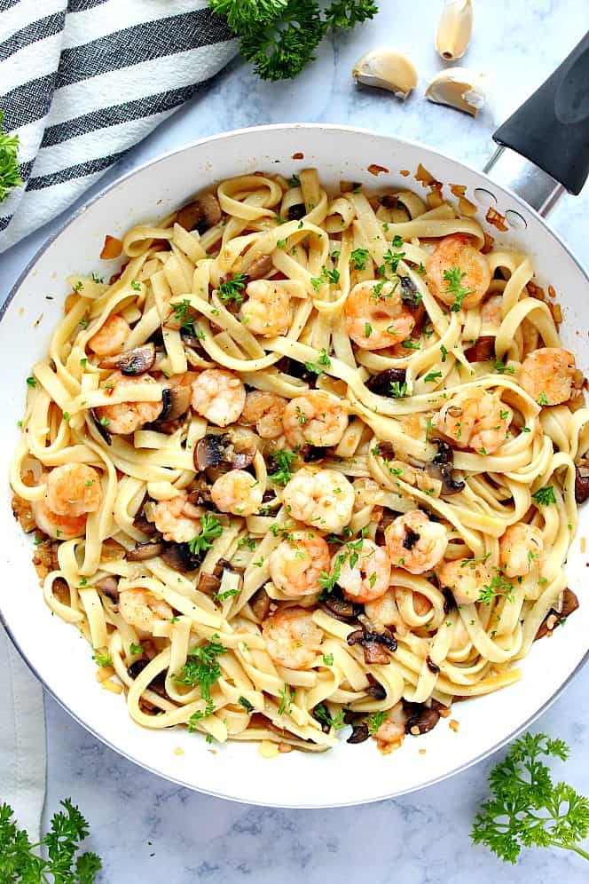 Overhead shot of fettuccine, mushrooms and shrimp in white skillet.