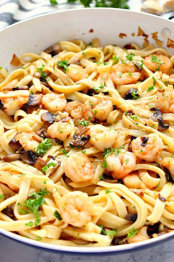 Close up shot of fettuccine shrimp mushroom pasta in white pan.