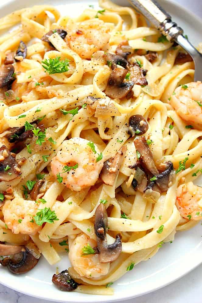 Overhead close up shot of fettuccine pasta with shrimp and mushrooms, served on white plate.