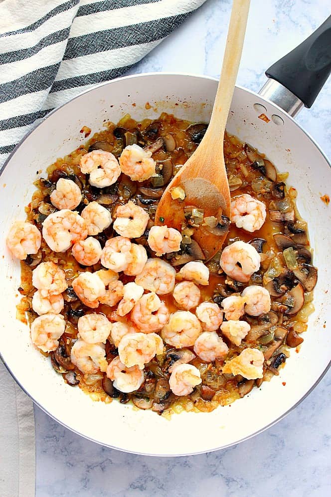 Overhead shot of white pan with mushroom sauce and cook shrimp.