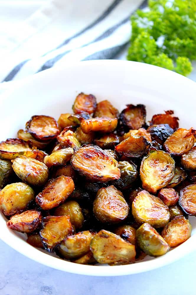 Close up side shot of roasted Brussels sprouts in white serving bowl. 