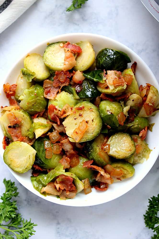 Overhead shot of Brussels sprouts with onions and bacon in white serving bowl. 