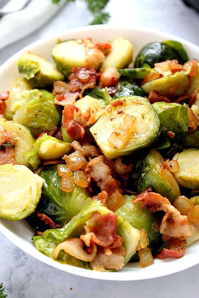 Instant Pot Bacon Brussels Sprouts Recipe - quick and easy side dish recipe with Brussels sprouts that are steamed and then sauteed with garlic, onion and crispy bacon. All in your Instant Pot! Close up shot of Brussels sprouts with bacon and onions, in white serving bowl.