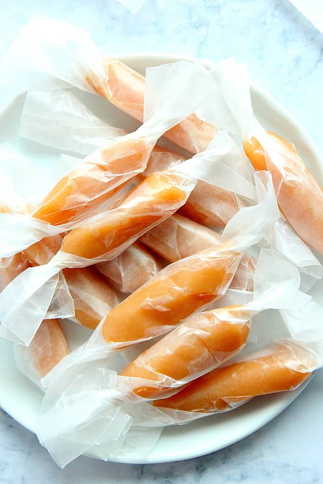 Overhead shot of caramels wrapped in wax paper, placed on white plate.