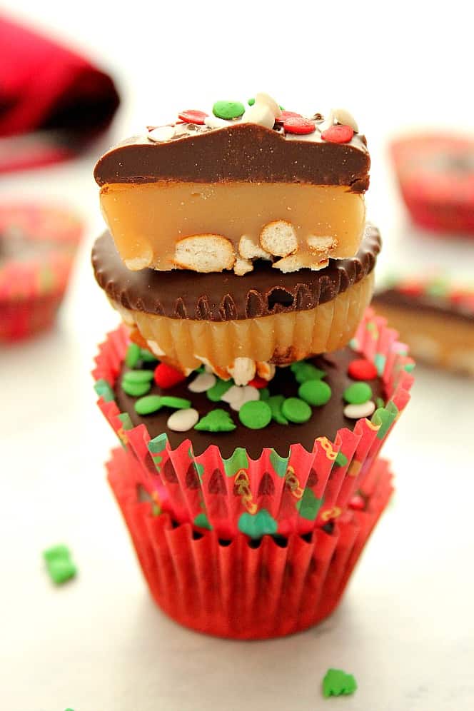 Chocolate Caramel Pretzel Cups Recipe - little sweet treats that are perfectly festive for the holidays! Crushed pretzels create a salty and crunchy crust for the gooey caramel layer, later topped with rich chocolate. Side shot of caramel cups stacked on each other, with one cut in half.