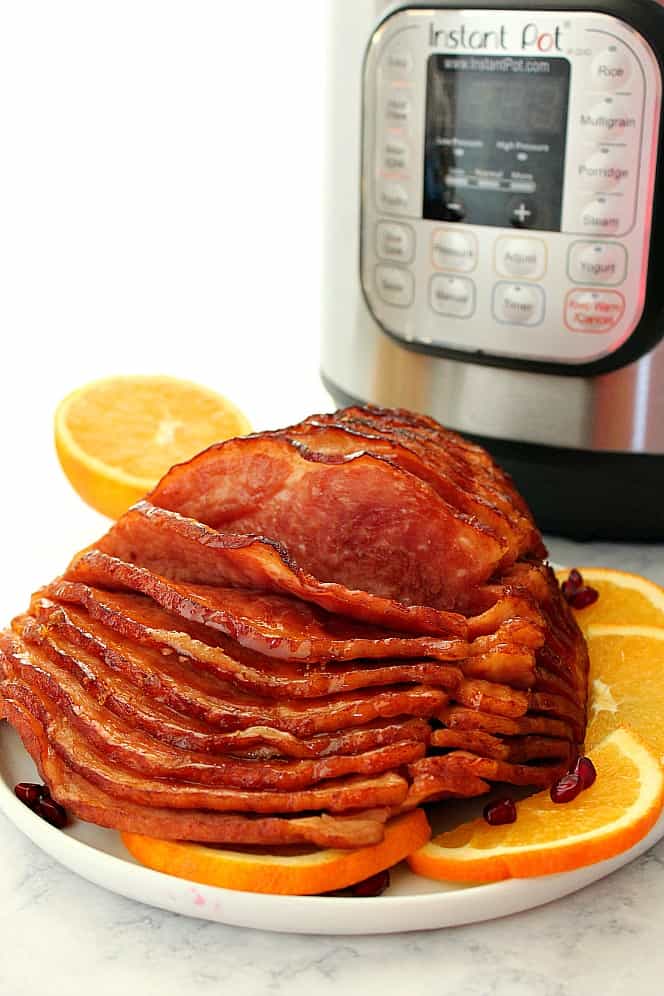 Side shot of spiral-cut ham on white plate with orange slices around it. 