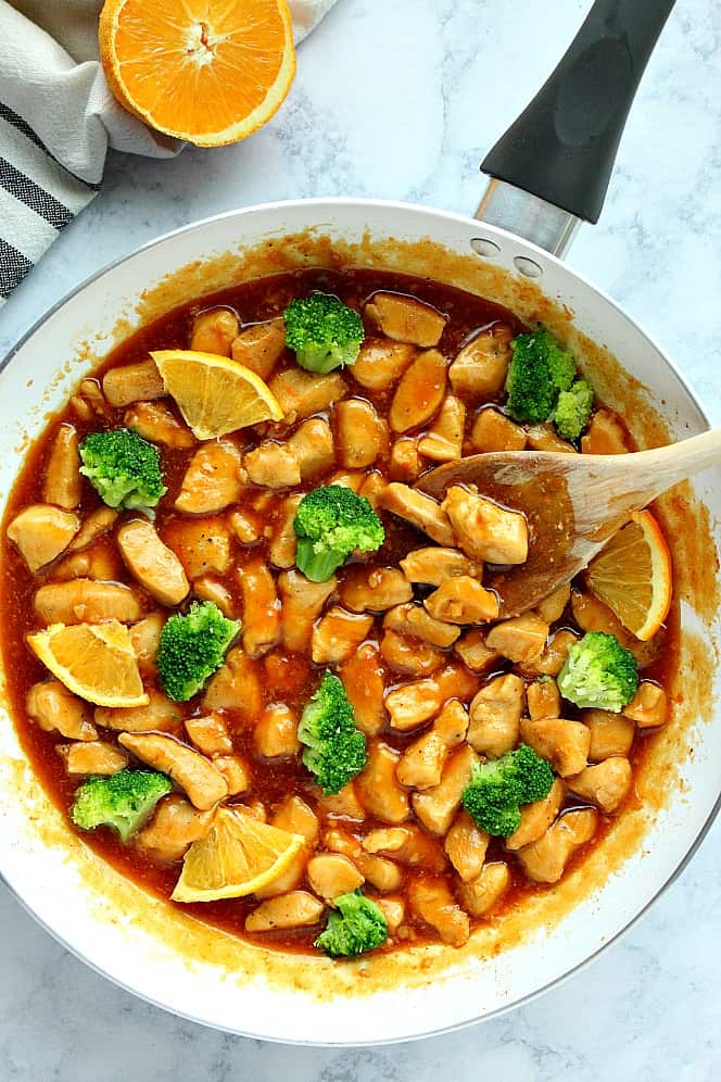 Overhead shot of chicken in bite size pieces in orange sauce in white skillet. 