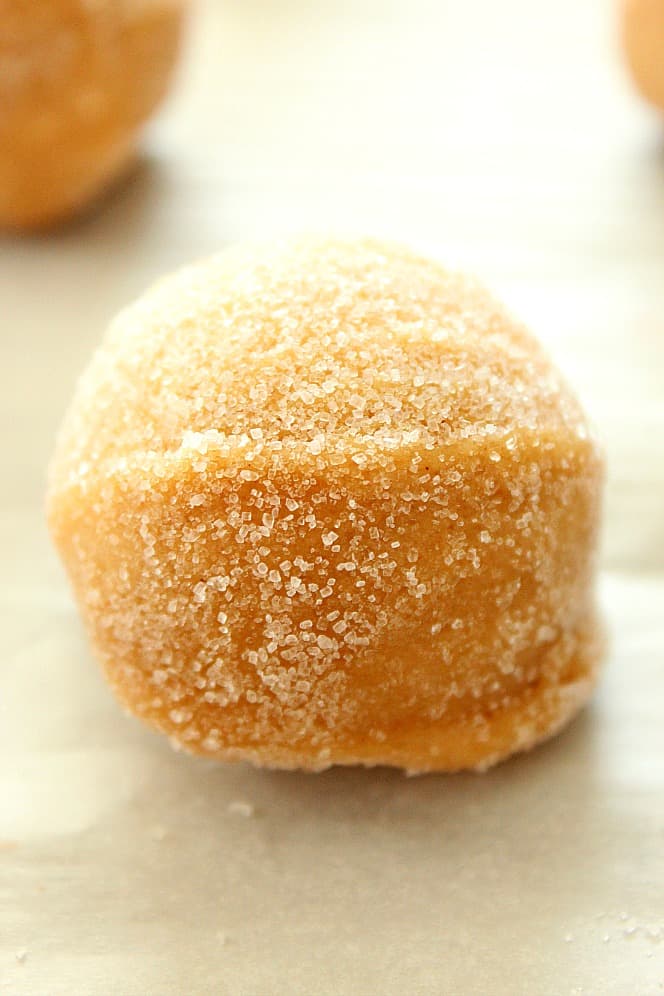 Close up shot of peanut butter cookie dough ball rolled in sugar, placed on baking sheet.