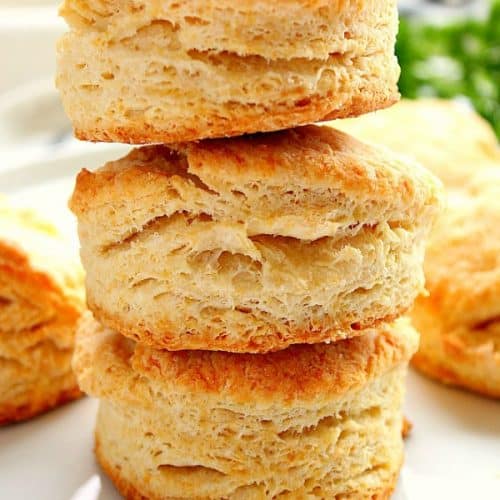 Flaky buttermilk biscuits stacked on white plate.