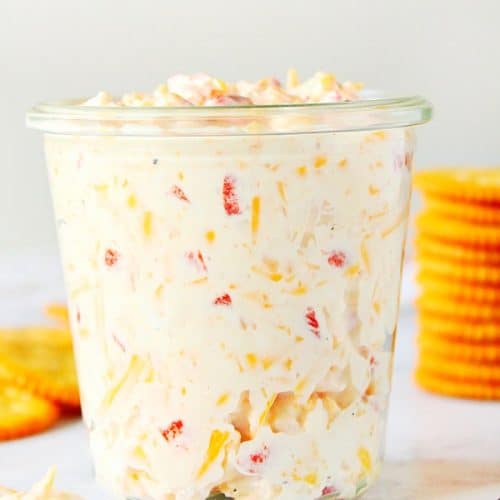 Pimento Cheese Spread in a glass jar, with crackers behind it.