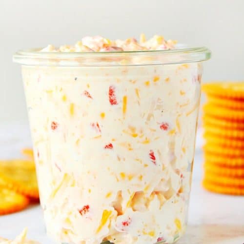 Pimento Cheese Spread in a glass jar, with crackers behind it.