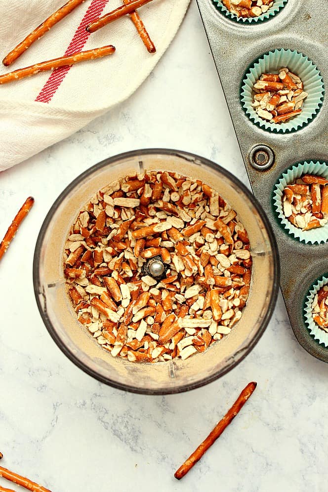 Overhead shot of pretzels crushed in mini food processor bowl and mini cupcake liners. 