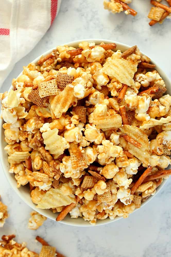 Sweet and Salty Caramel Popcorn Mix made with popcorn, pretzels, Chex cereal, nuts and potato chips, all coated in caramel. Caramel popcorn with pretzels and potato chips in large white bowl.