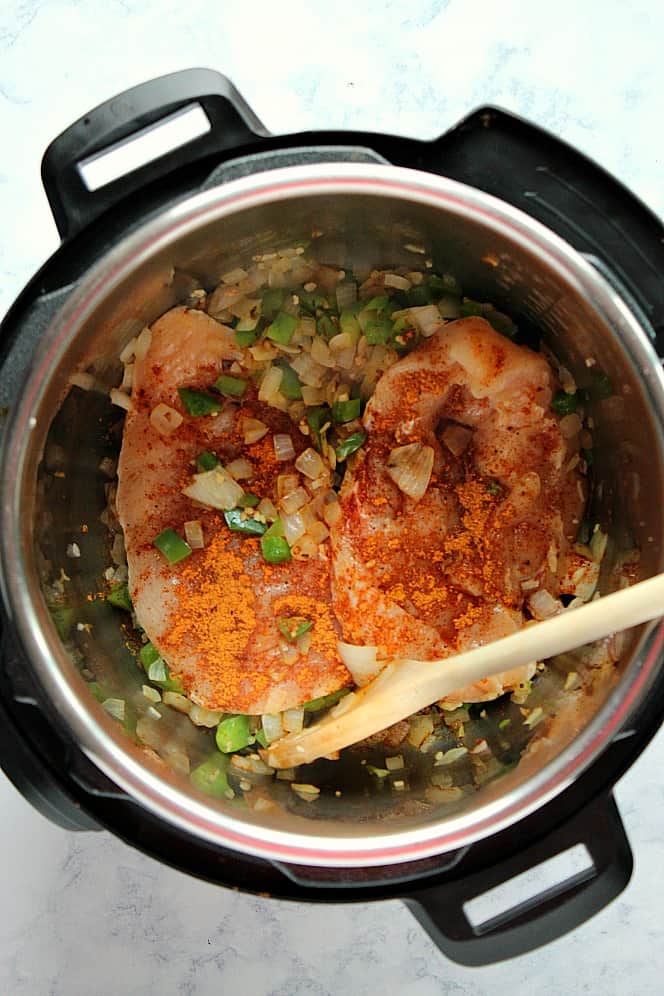 Overhead shot of onions and green peppers sauteed, with two chicken breast in the Instant Pot. 