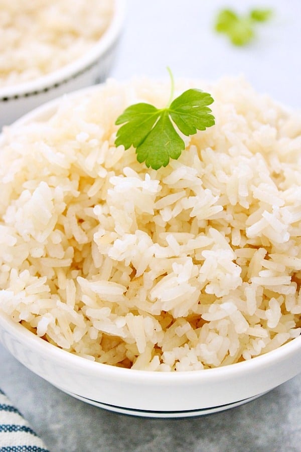 Cooked rice in a white bowl with a parsley leaf on top.