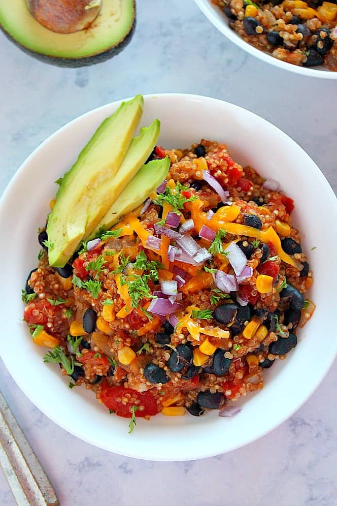 Overhead shot of quinoa with black beans, tomatoes, cheese and avocado slices in white bowl.