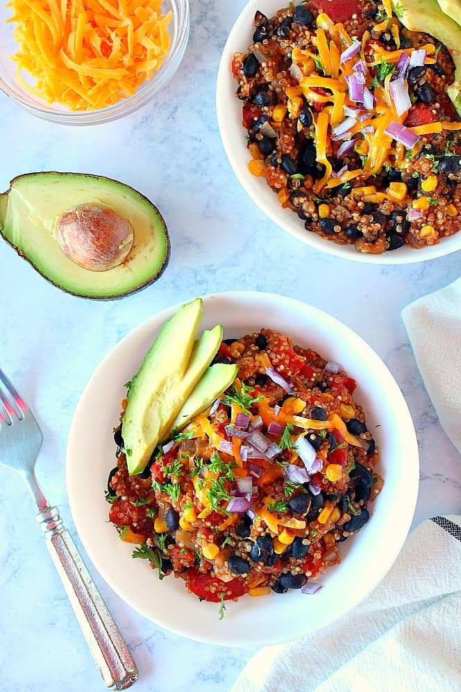 Overhead shot of two bowls of Mexican quinoa with shredded cheese, red onions and sliced avocados on top.