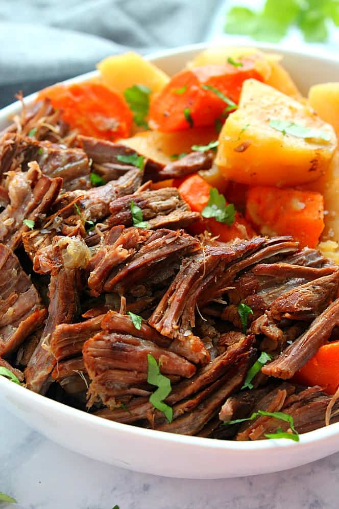 Close up shot of pot roast, potatoes and carrots in white bowl. 