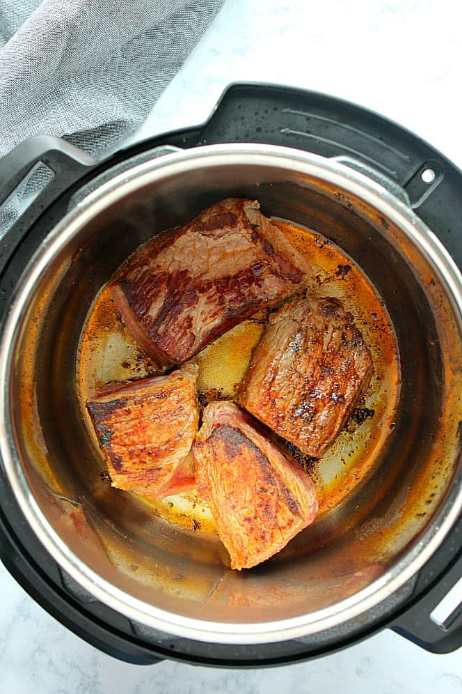 Overhead shot of 4 pieces of pot roast beef seared in the Instant Pot. 