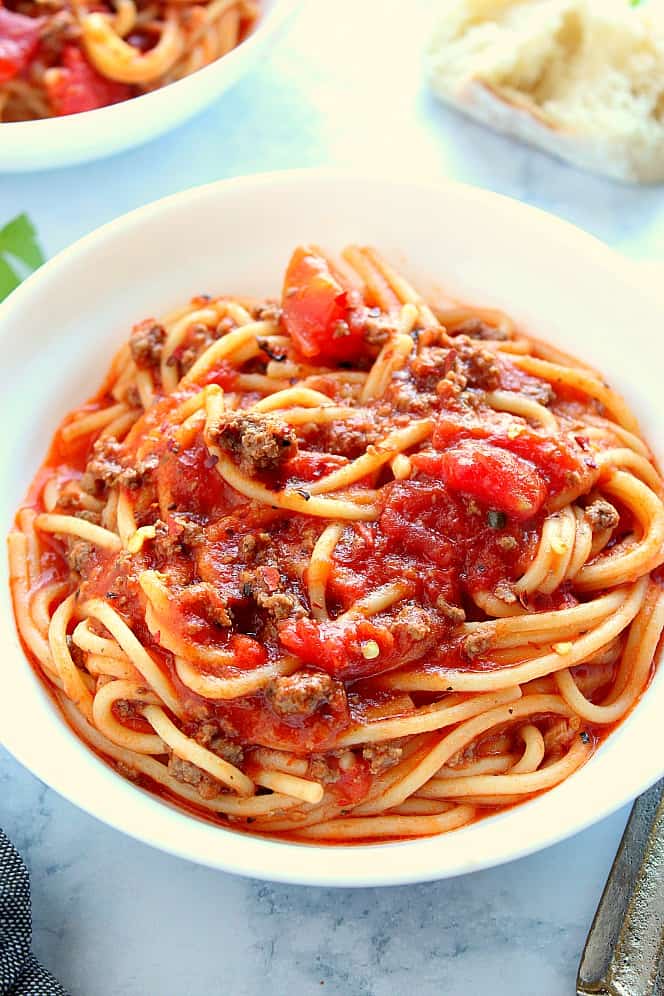 Spaghetti in a white pasta bowl on a marble board.