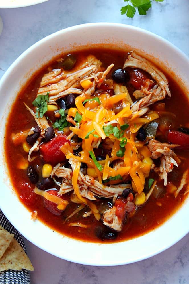 Overhead shot of white bowl filled with chicken tortilla soup topped with cheddar cheese and cilantro.