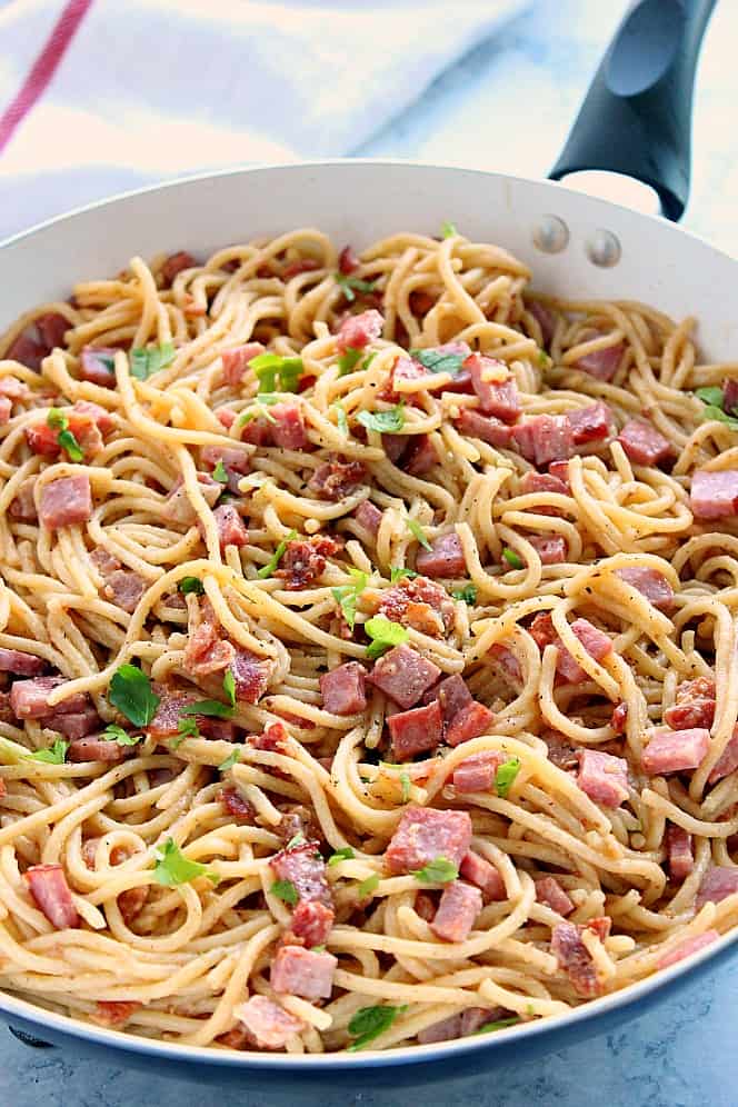 Side shot of spaghetti carbonara in white skillet.