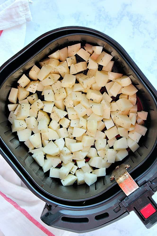 Overhead shot of potato chunks in the basket of an air fryer. 
