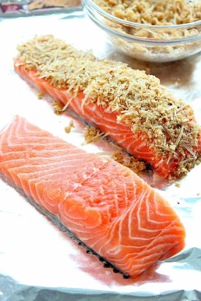 Side shot of two salmon fillets on aluminum foil lined baking sheet, one fillet with breadcrumb Parmesan crust on top.