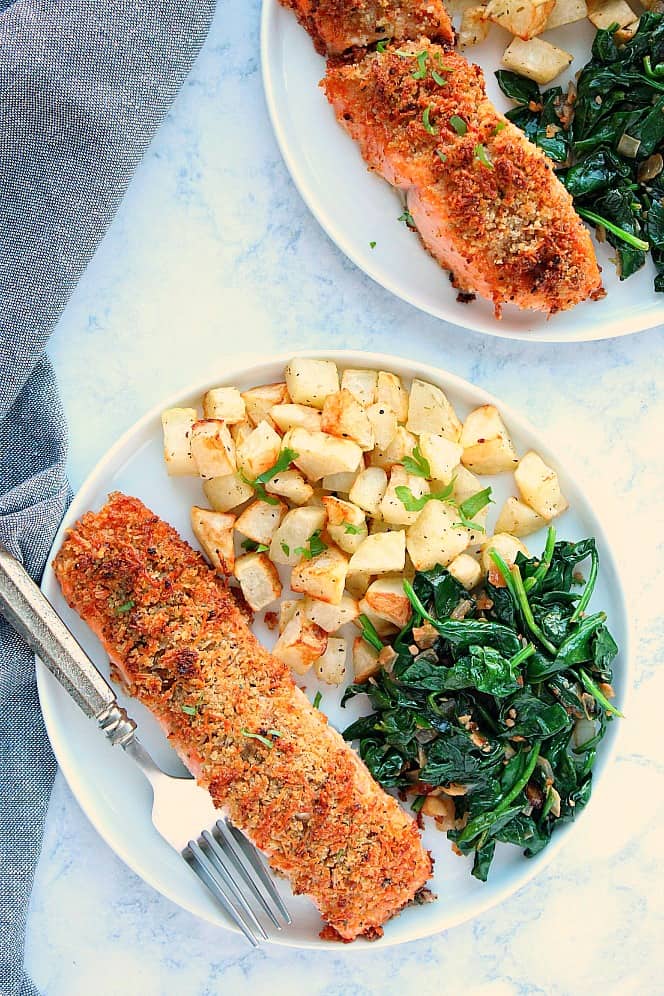 Overhead shot of two plates with crusted salmon, potatoes and spinach. 