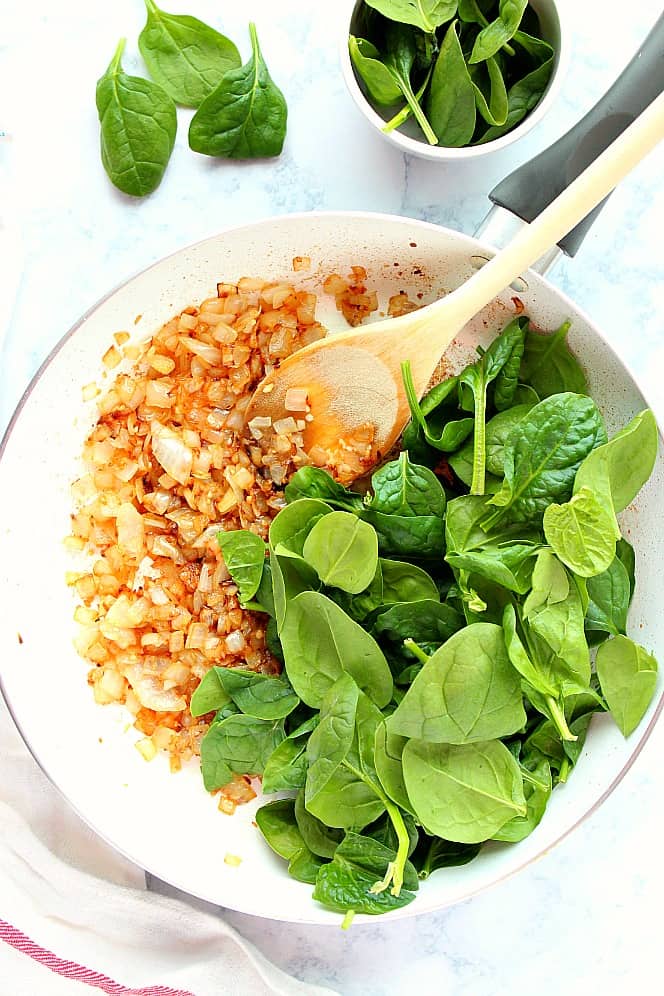 Overhead shot of sauteed onion and fresh spinach in pan. 