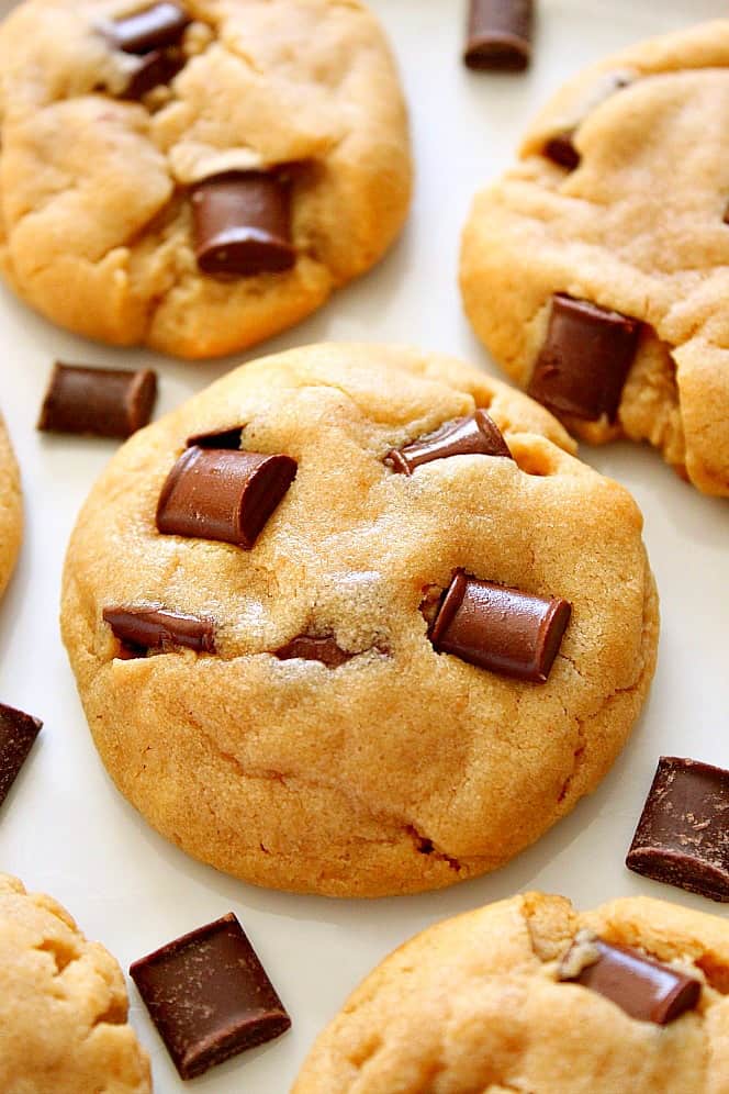 Close up shot of peanut butter chocolate chunk cookie on white board, other cookies and chocolate chunks arranged around it.