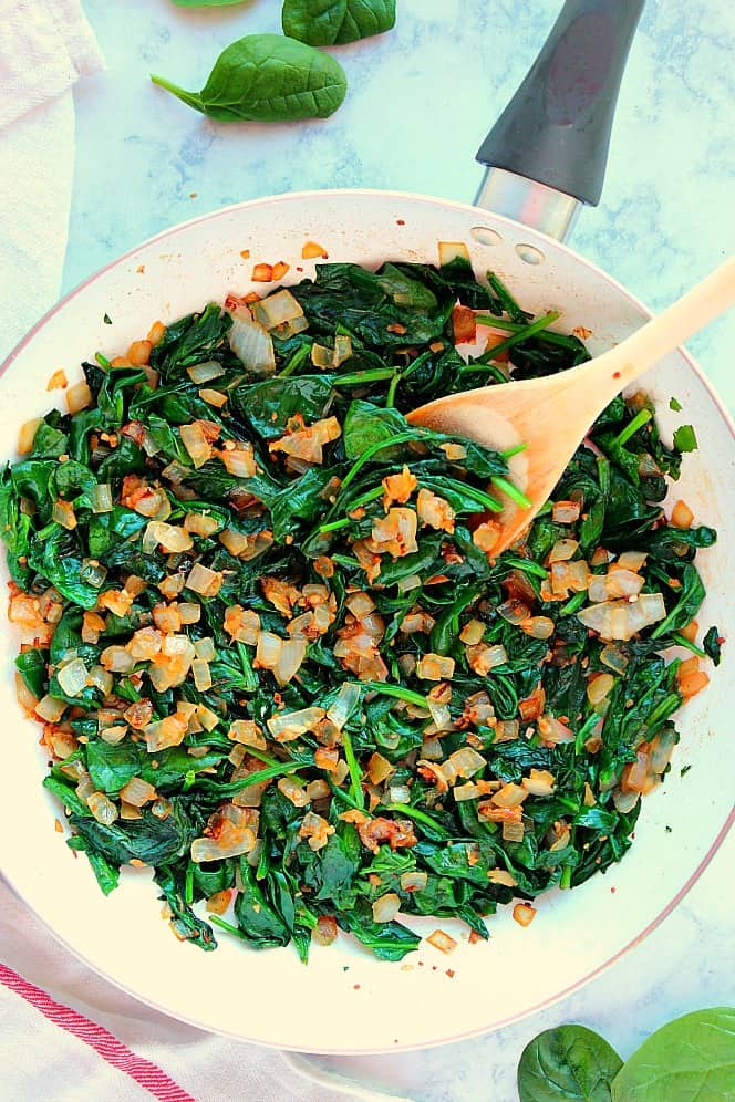 Overhead shot of sauteed spinach with onion in white skillet.