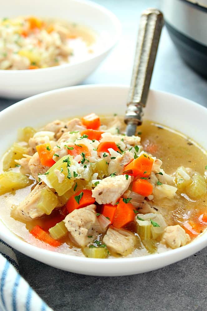 Side shot of chicken and rice soup in white bowl, another bowl and Instant Pot in the background.