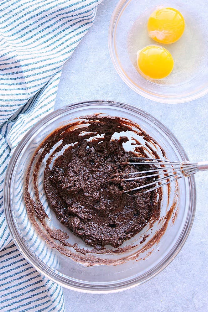 Overhead shot of chocolate sugar mixture in glass bowl, eggs in another bowl.