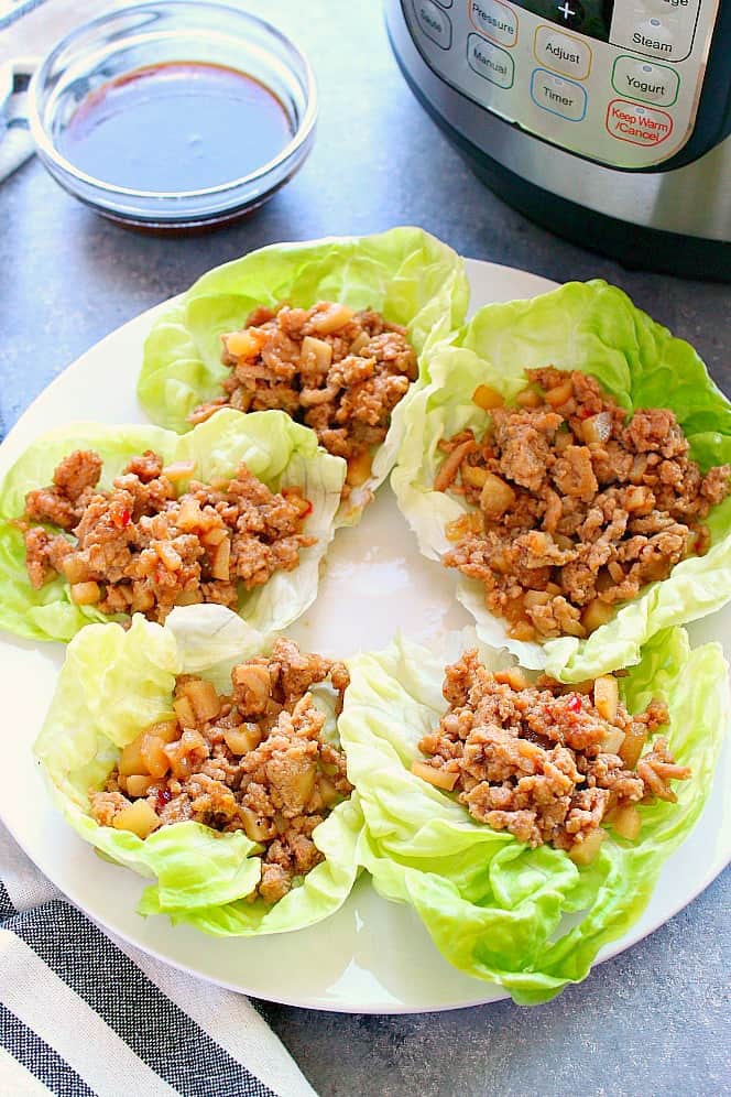 Side shot of 5 lettuce wraps with ground chicken on white plate, next to the Instant Pot. 