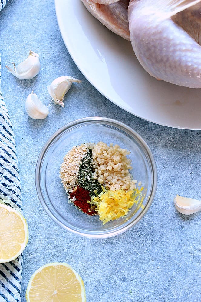 Overhead shot of seasoning mix in a small glass bowl, with whole chicken on plate in the background.