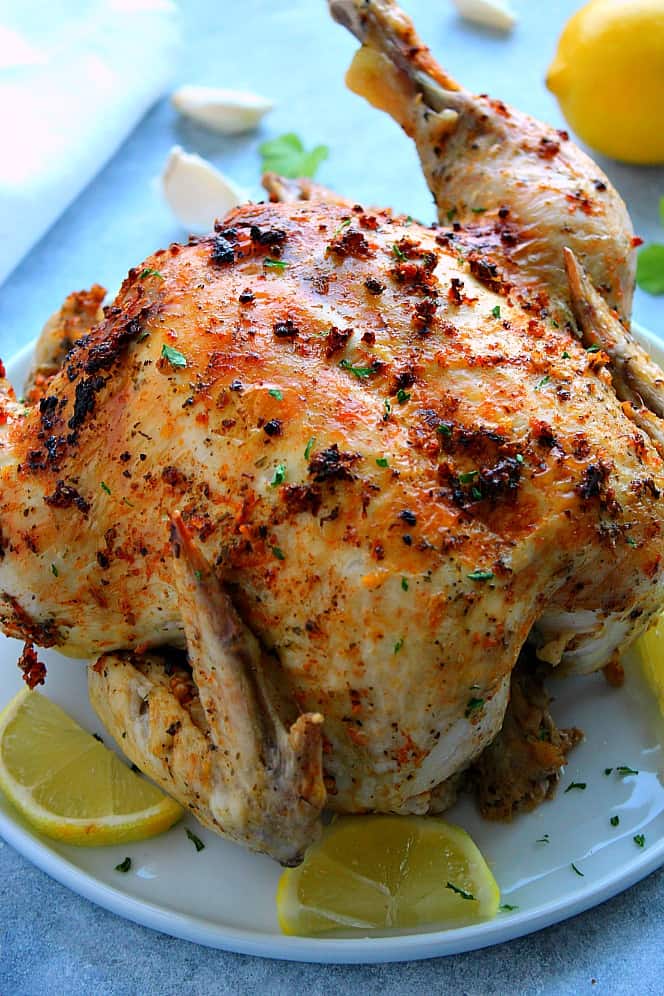 Side shot of roasted chicken with lemon slices on white plate.