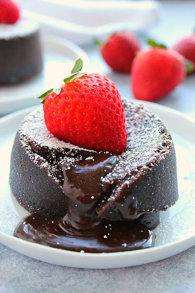 Side shot of chocolate lava cake with gooey center, strawberry on top, set on white plate.